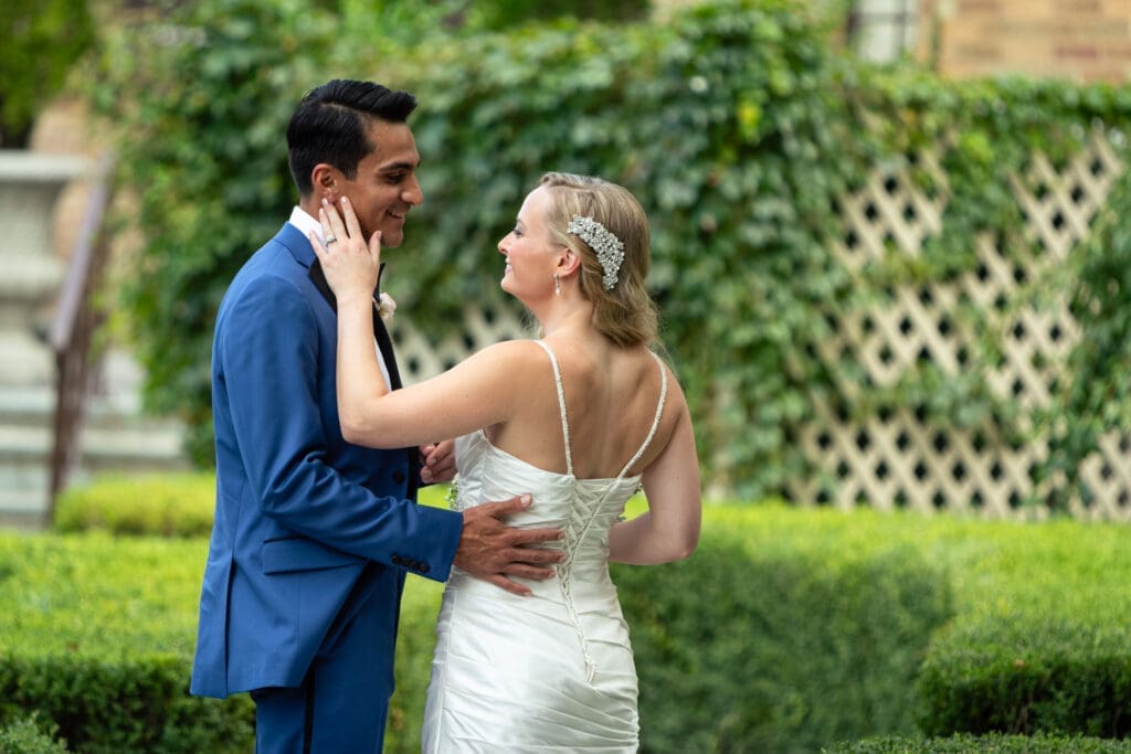 Bride puts her hand on the groom's face as they smile at each other at Hotel Baker.