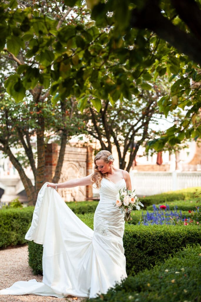 Bride holding up her train in the garden at Hotel Baker.