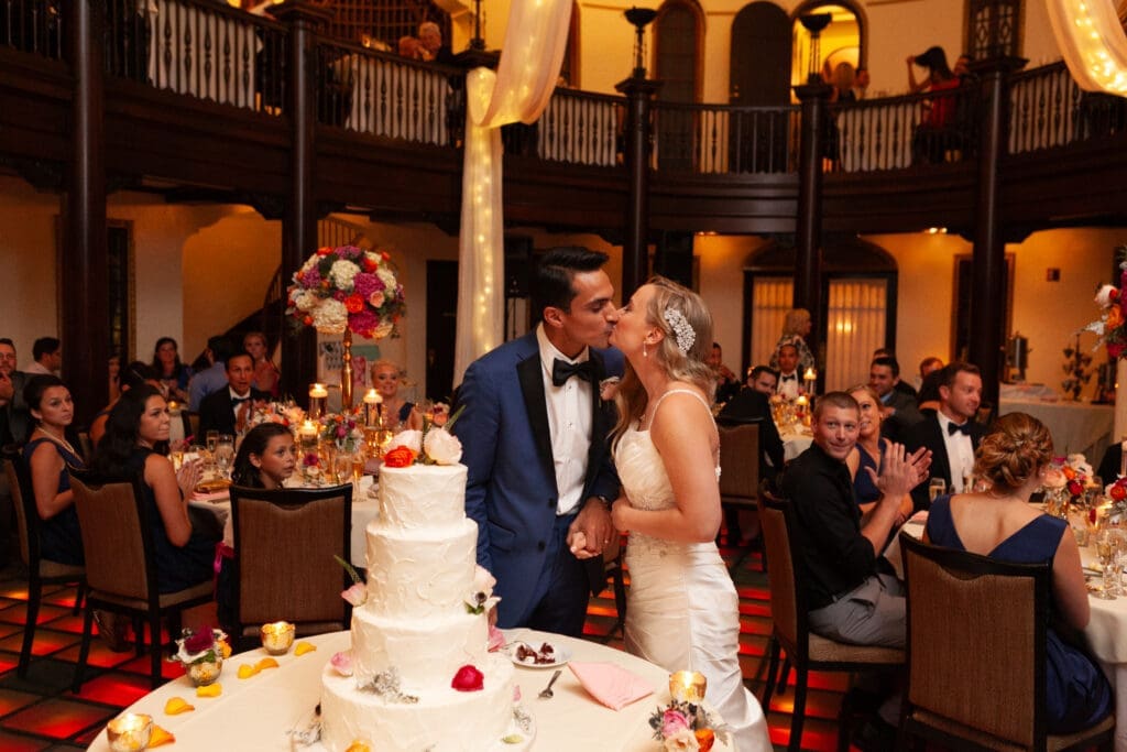Bride and groom kiss by their wedding cake in the Rainbow Room at Hotel Baker.