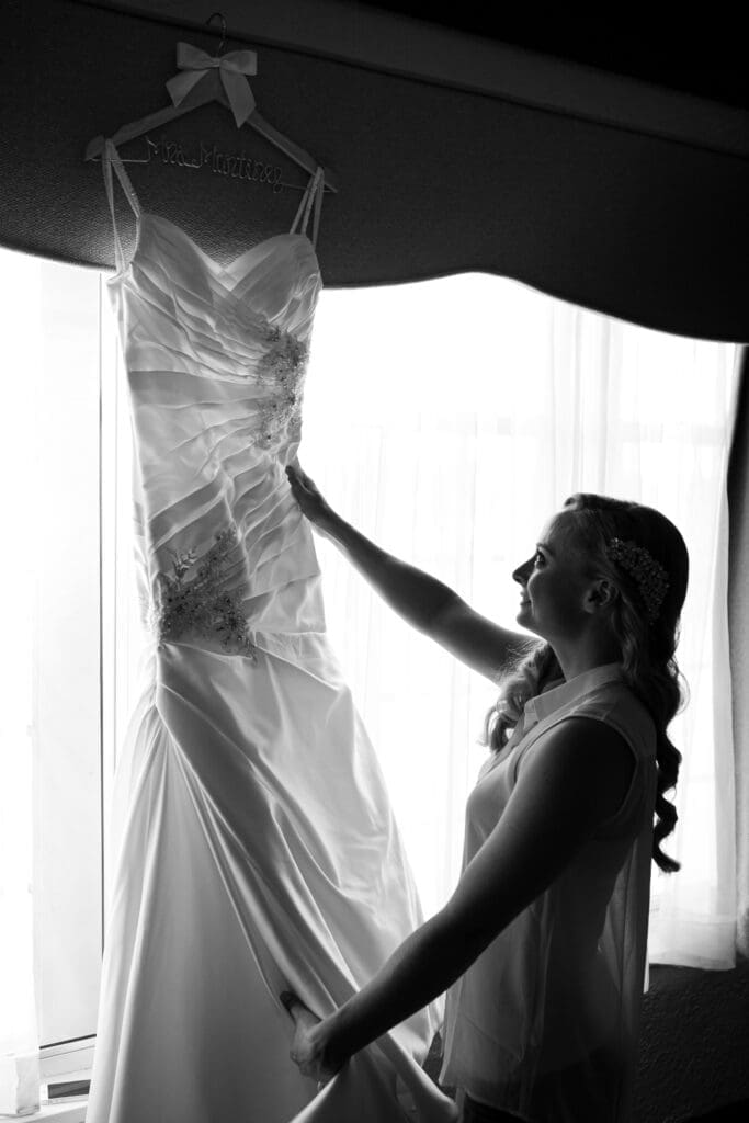 Beautiful bride holding her dress in front of a window at Hotel Baker.