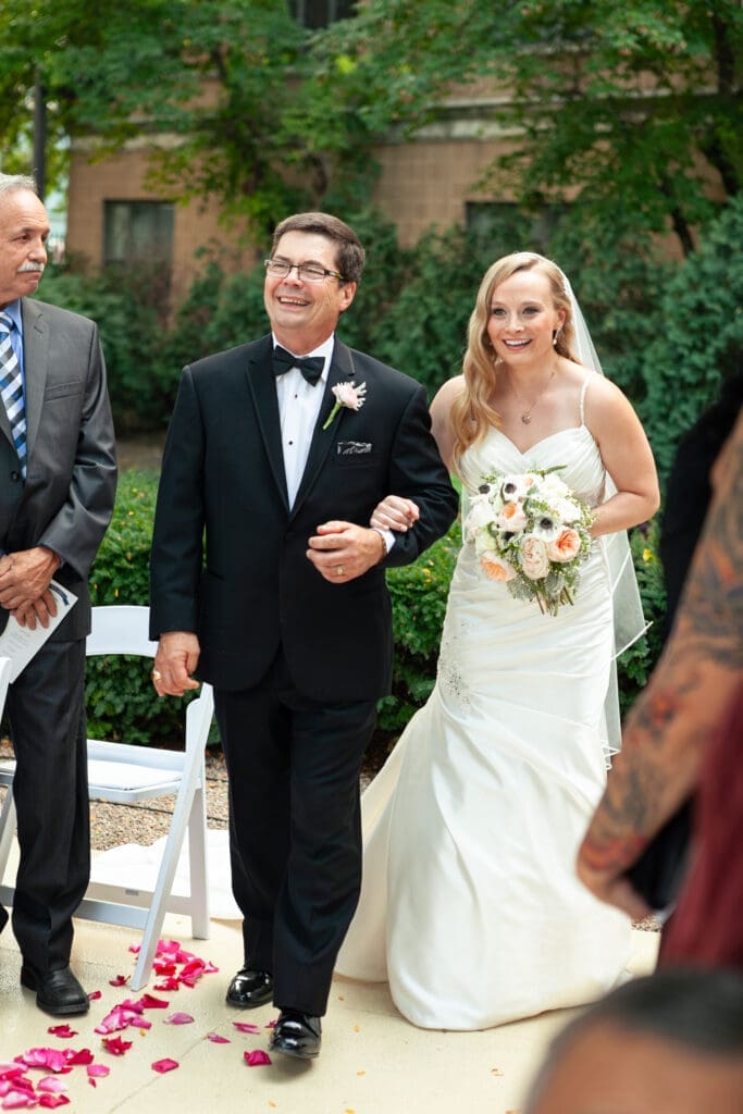 Bride and her father smiling and laughing while being walked down the aisle for her wedding.
