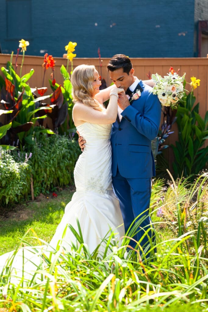 Groom kissing smiling bride's hand with her flowers at Hotel Baker.