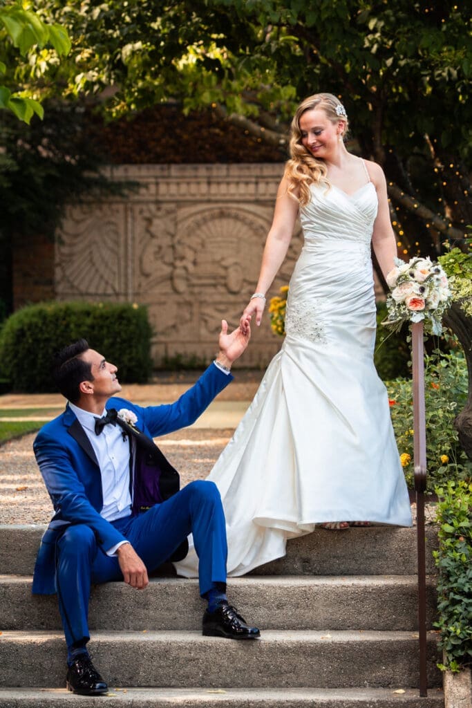 Groom sitting on steps holding his bride's hand at Hotel Baker while gazing at each other.