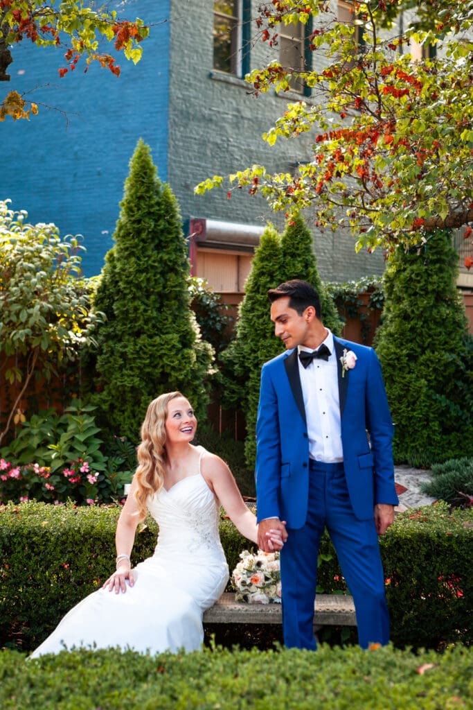 Bride sitting and groom standing in the garden at Hotel Baker laughing and looking at each other.