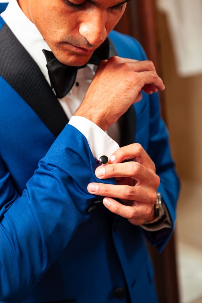 Groom in blue tuxedo fixes his cufflinks at hotel