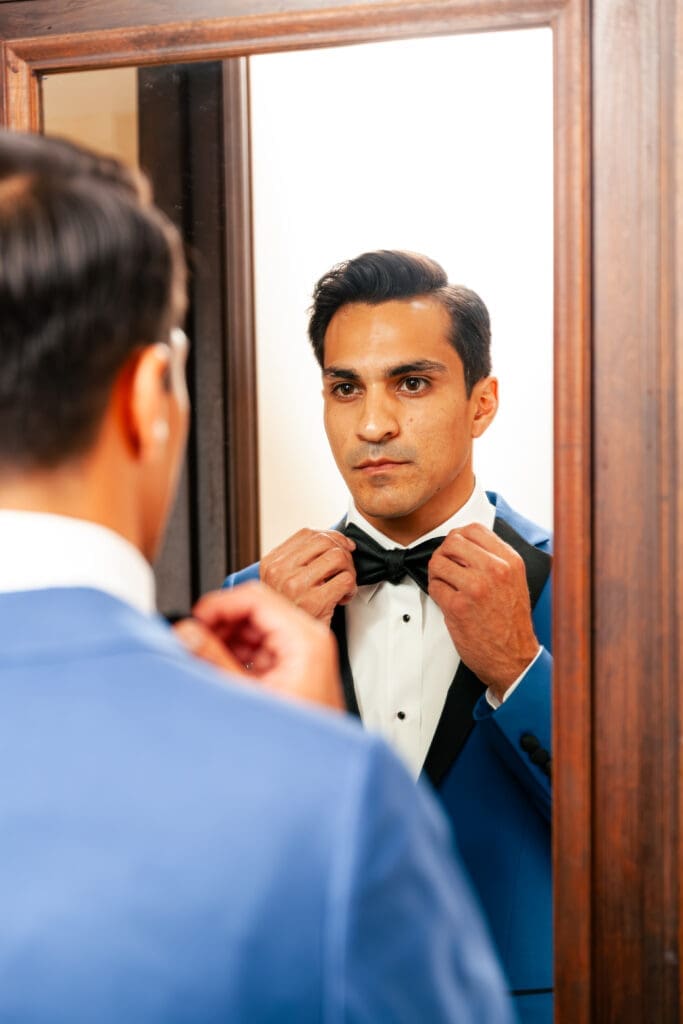 Handsome Groom looks at himself in the mirror and fixes his bow tie and his tuxedo in Hotel Baker Saint Charles Illinois.