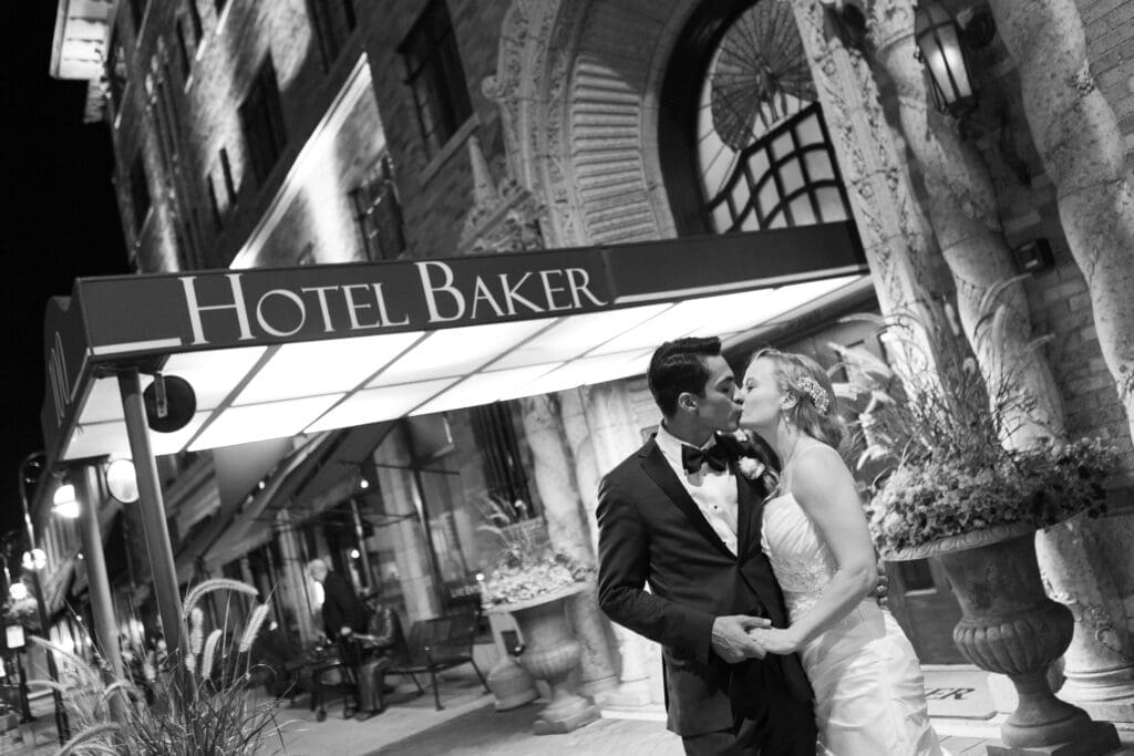 Bride and groom kissing at night in front of Hotel Baker at the end of their wedding day.