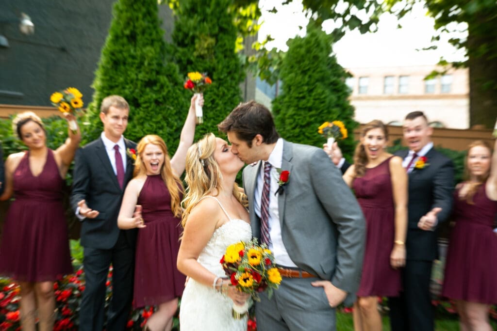Action shot of bride and groom kissing with bridal party cheering.