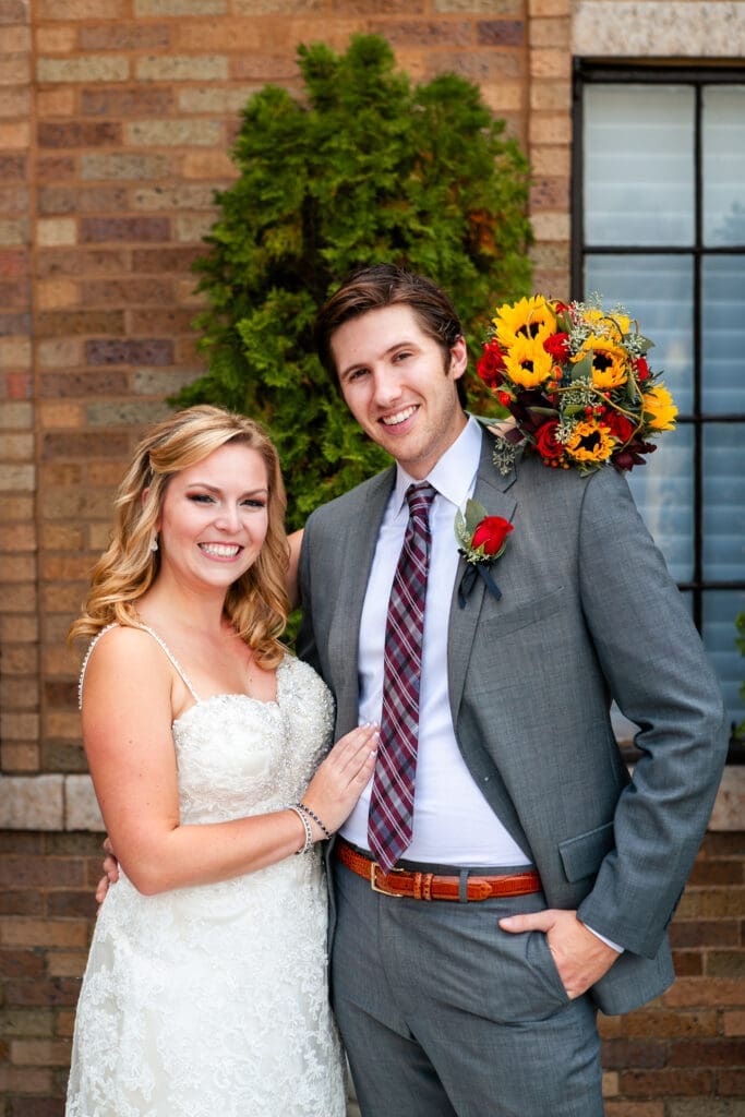 Bride holding flowers on groom's shoulder as they pose for a photo at Hotel Baker St. Charles.