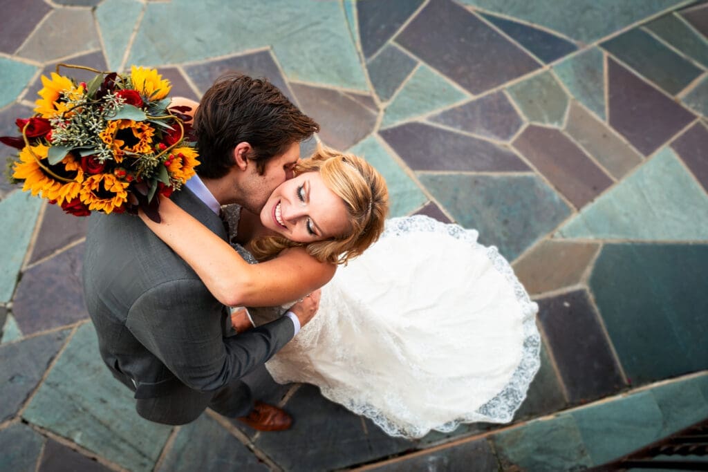Looking down on bride and groom kissing her neck with flowers at Hotel Baker