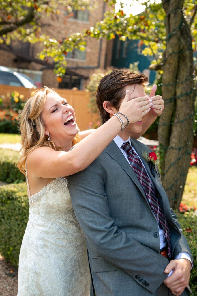 Bride laughing as she holds her hands over the groom's eyes before their first look together in the English garden at Hotel Baker.