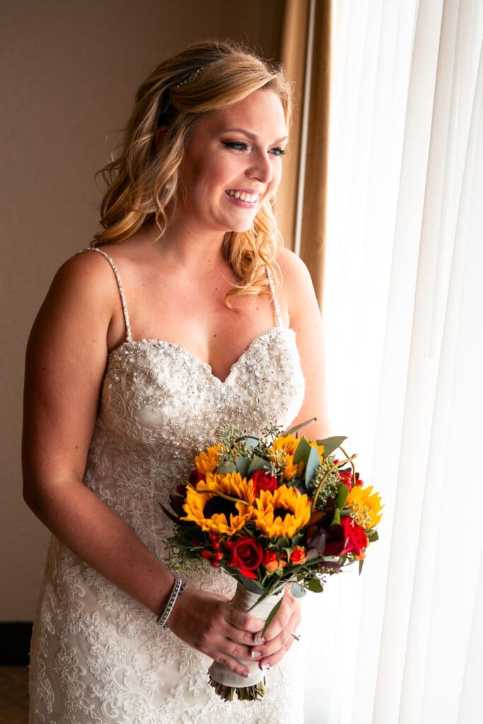 SMiling bride looking out the window on her wedding morning in the bridal suite at Hotel Baker St. Charles.