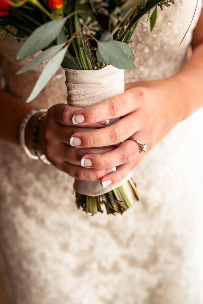 Closeup of bride's hands with her engagement ring holding her flowers.