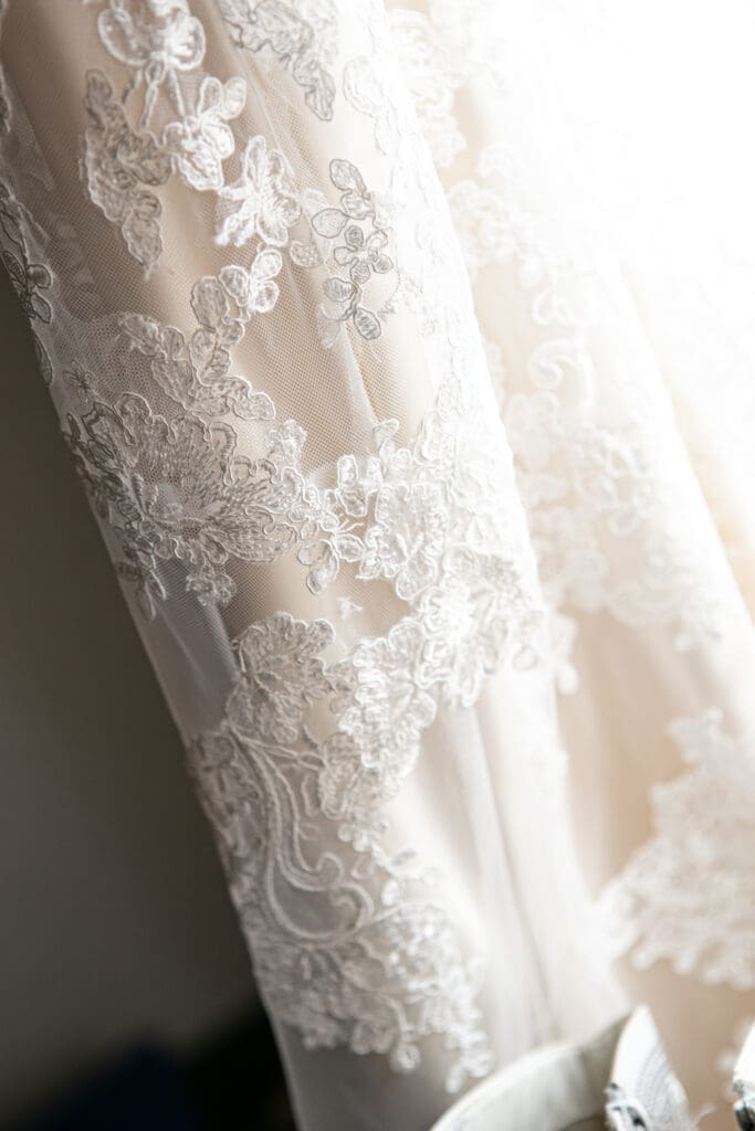 Close up detail of brides dress hanging in natural lit window at Hotel Baker bridal suite.
