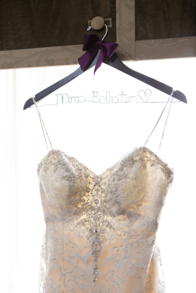 Mrs. Bolster wedding dress hanging from a custom wire hanger with her new last name on it.
