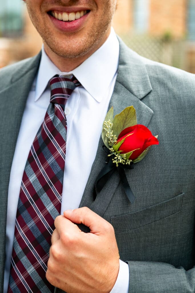 Groom clutching his suit jacket as he smiles and show off his boutonniere.