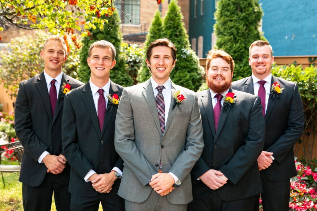 Straight on formal pose with groom and groomsmen smiling.