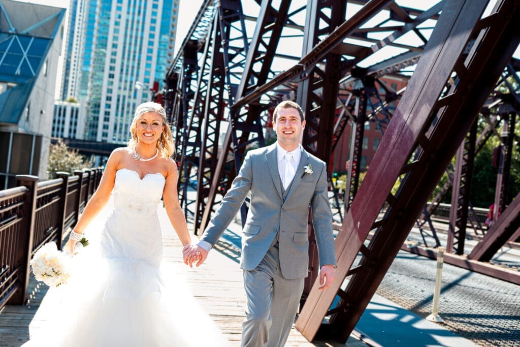 Bride and groom walking on a bridge in Chicago smiling on their wedding day in the bright sun.