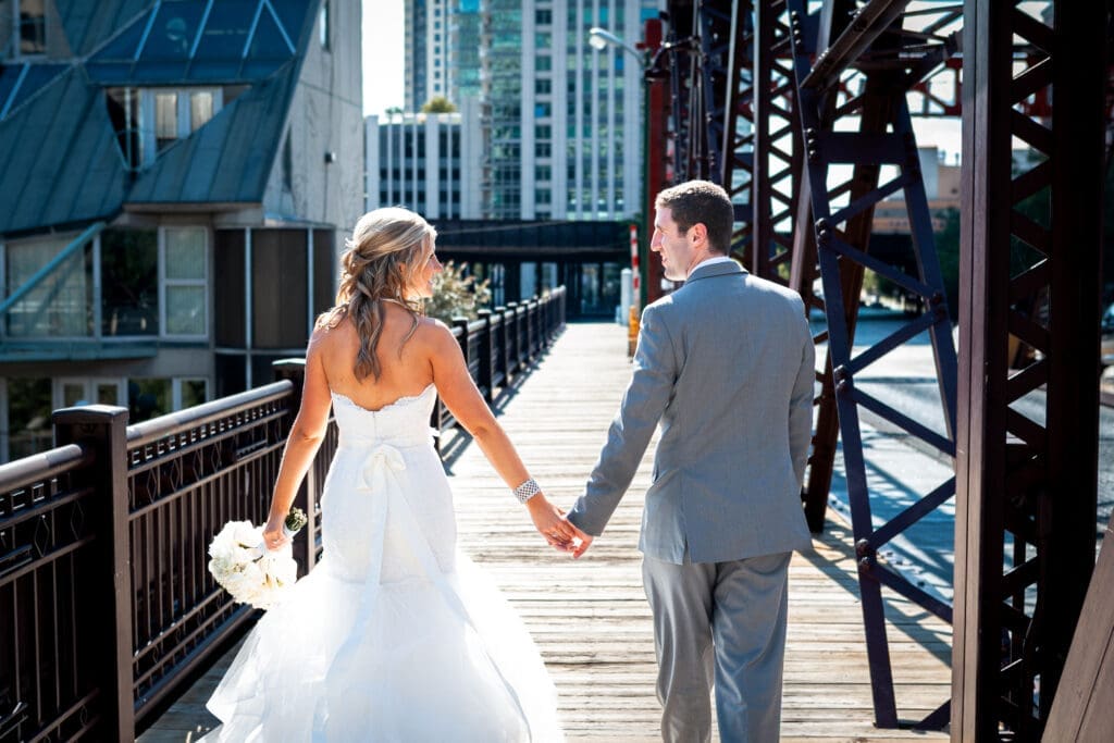 Bride and groom walking away holding hands on the Kinzie and Canal railroad bridge in Chicago.