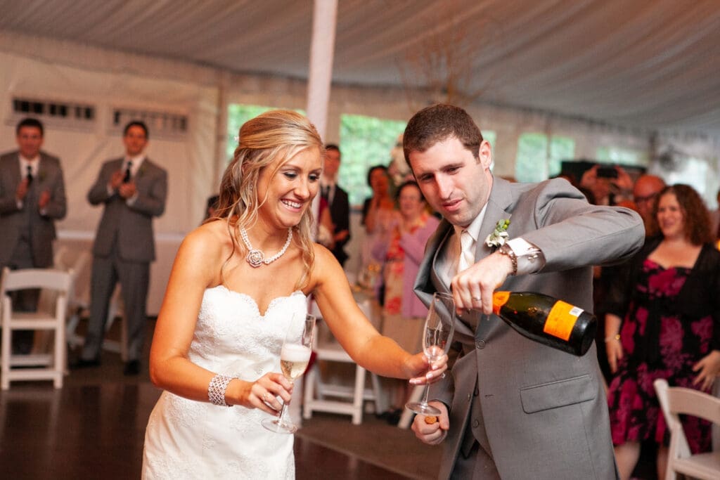 Groom pours champaign into a glass his bride is holding as they celebrate their marriage at their wedding reception.