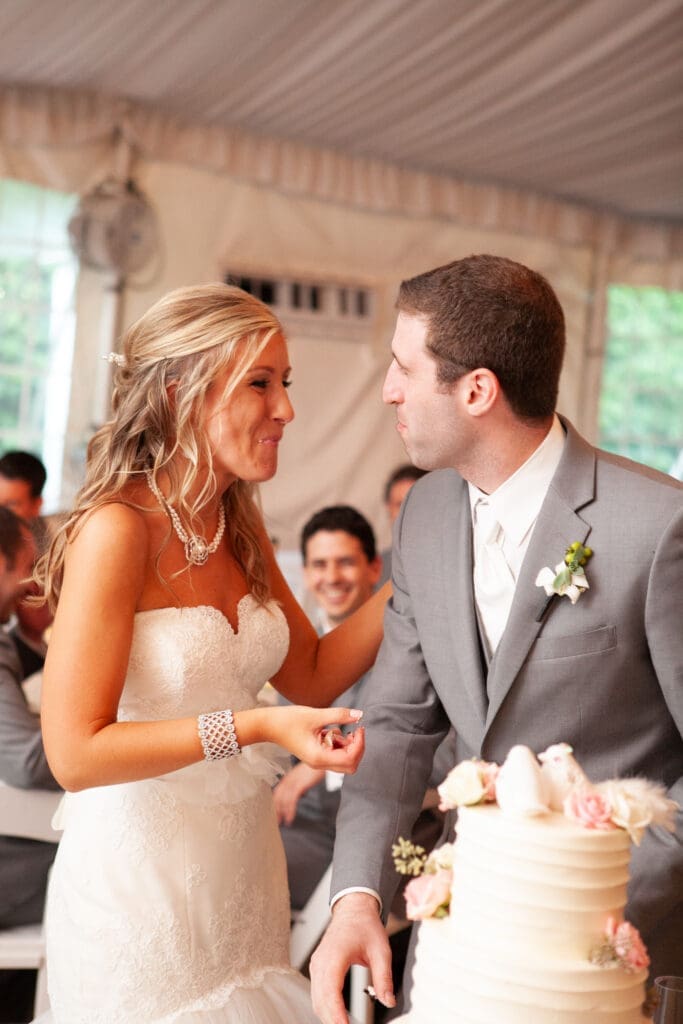 Bride and groom smiling at each other with mouths full of cake at their private estate wedding reception in Chicago.