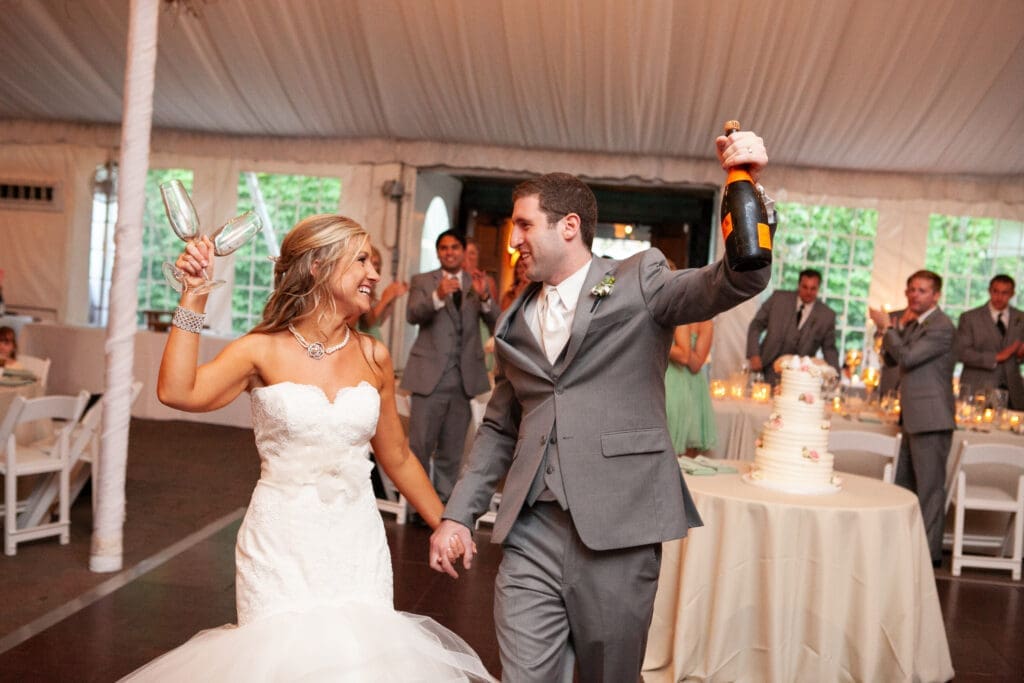 Bride and groom entrance with champaign at a private estate wedding reception with glasses and champaign raised high into the air.