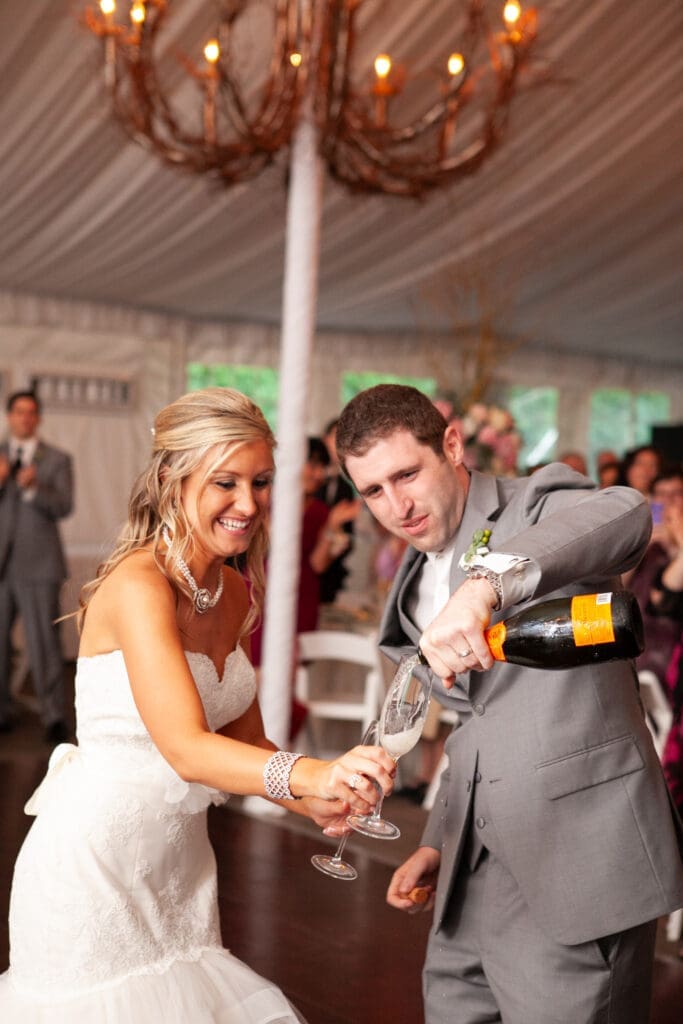 Groom pours champaign into a glass his bride is holding as they celebrate their marriage at their wedding reception in Chicago at a private estate.