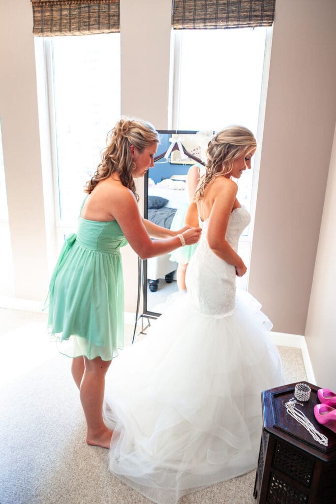 Bridesmaid fixing bride's dress at the Langham Chicago bridal suite.