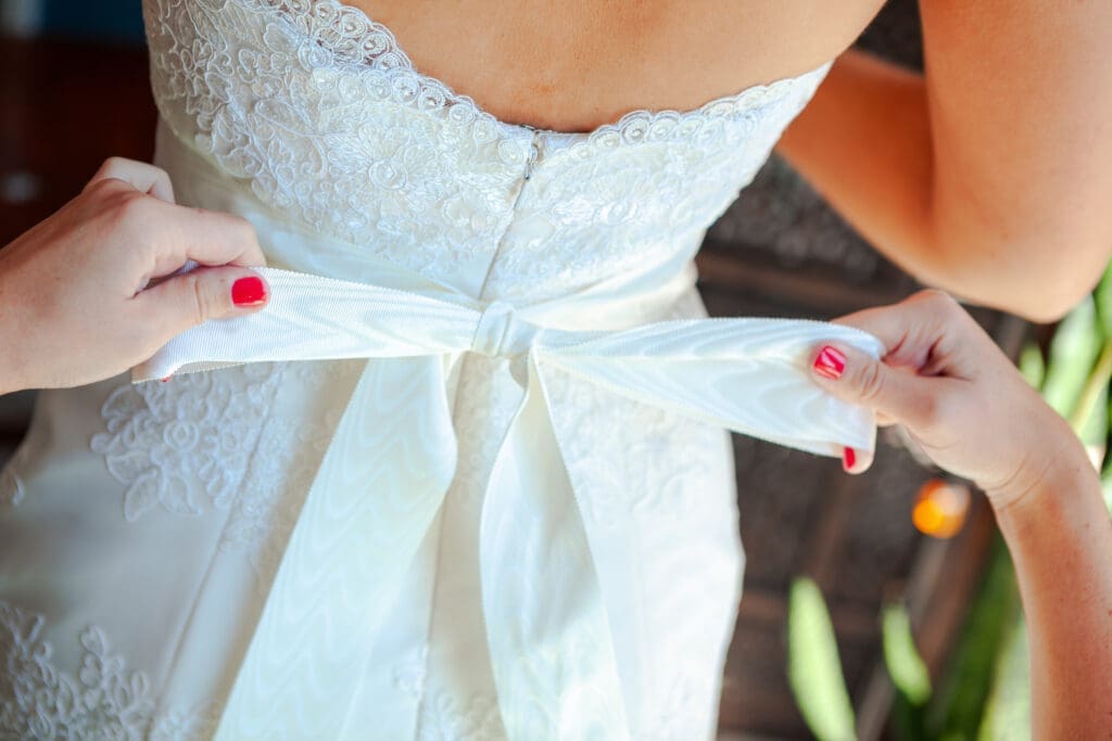 Bridesmaid tying the bride's ribbon bow on her wedding dress.
