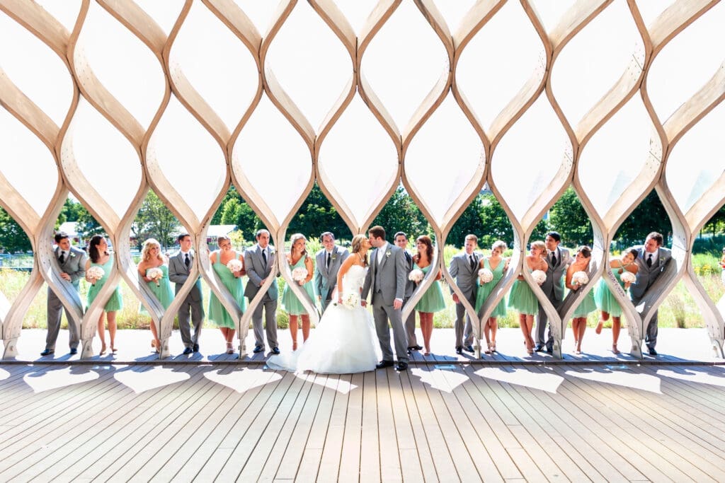 Bride and groom kissing with large bridal party around them at the North pond Lincoln Park Zoo Chicago.