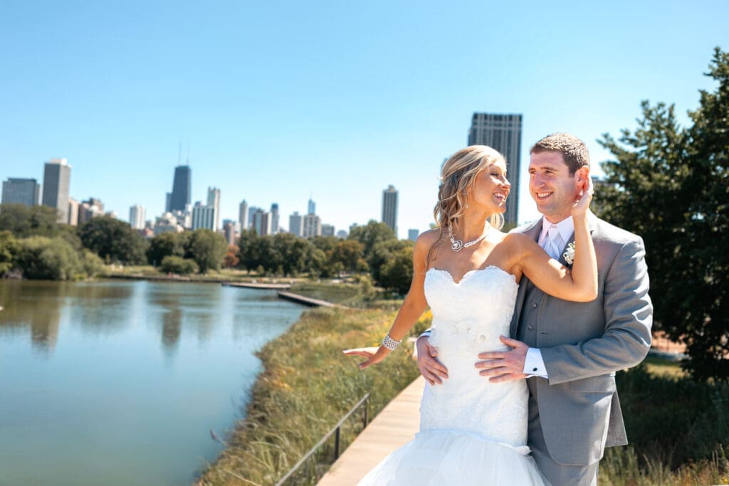 Bride smiling at groom with ehr arm up around him and the Chicago skyline behind them at Lincoln Park Zoo.
