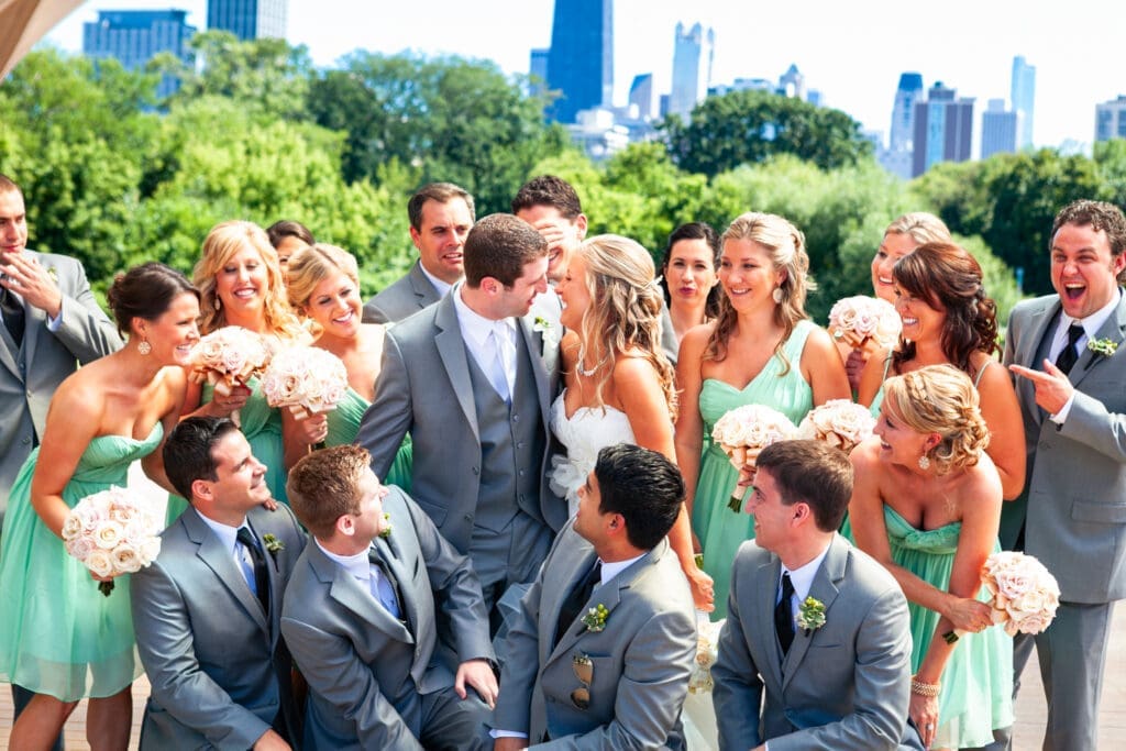 Bride and groom being intimate with bridal party around them at Lincoln Park zoo with Chicago skyline backdrop.