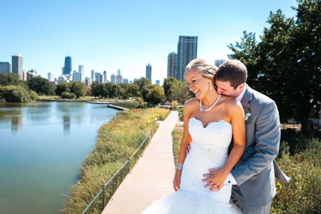 Groom kissing bride's neck at Lincoln Park Zoo Chicago skyline.