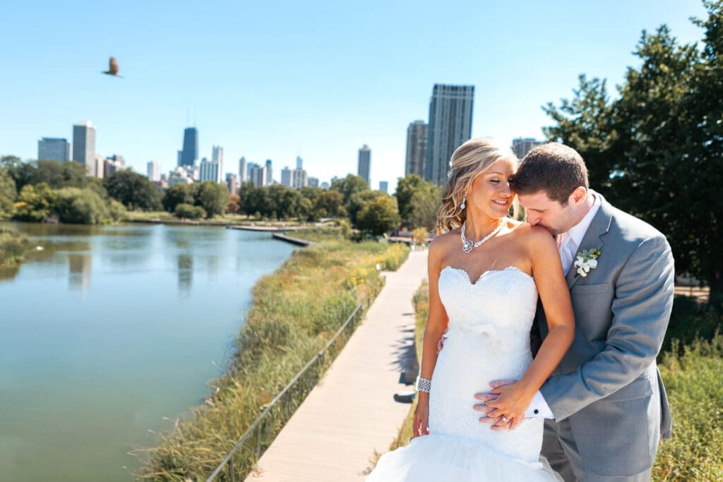 Groom kissing bride's shoulder at Lincoln Park Zoo with the Chicago skyline behind them.